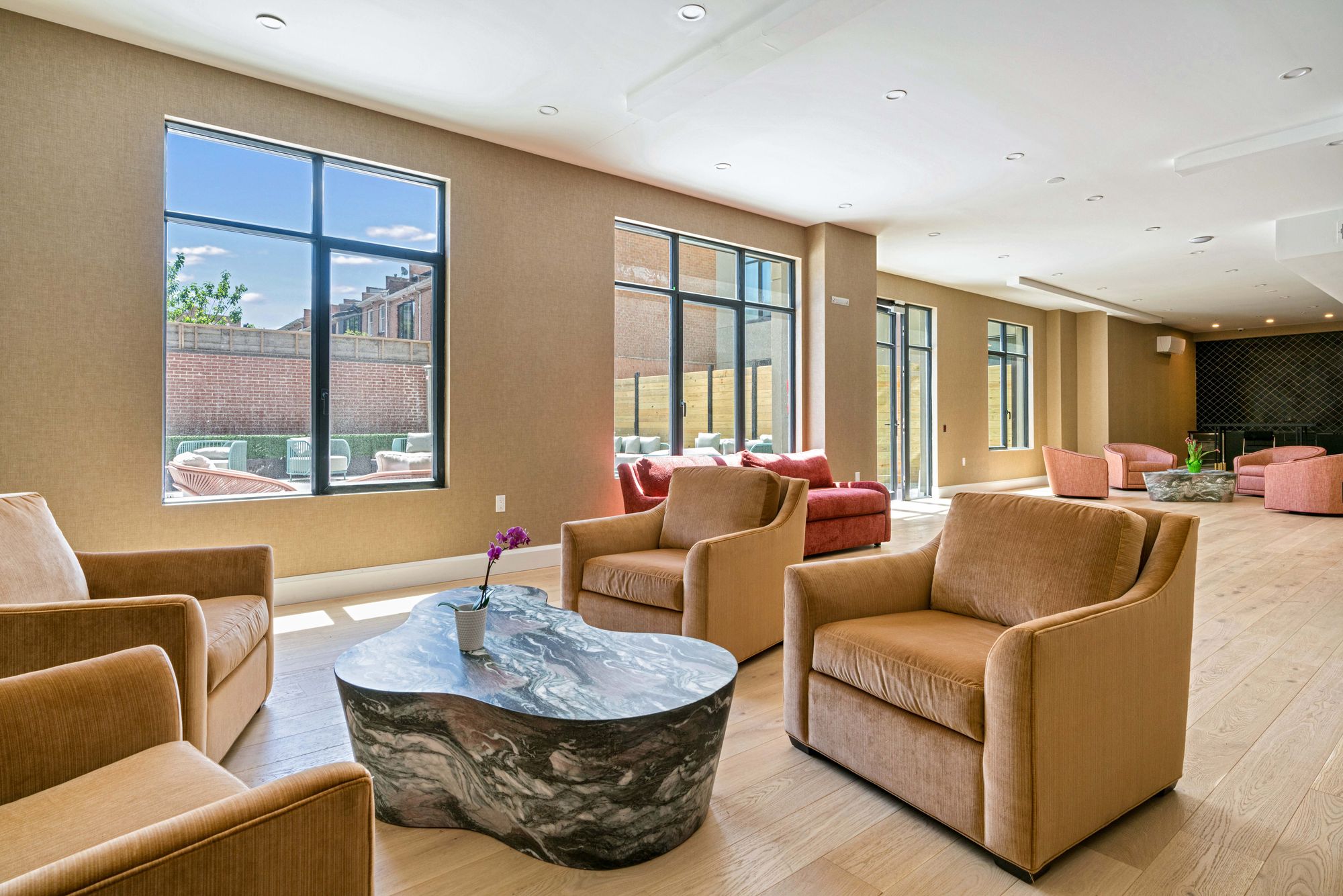 Sunlit resident lounge and co-working space with velvet armchairs and floor-to-ceiling windows at 875 Fourth Avenue in Sunset Park Brooklyn